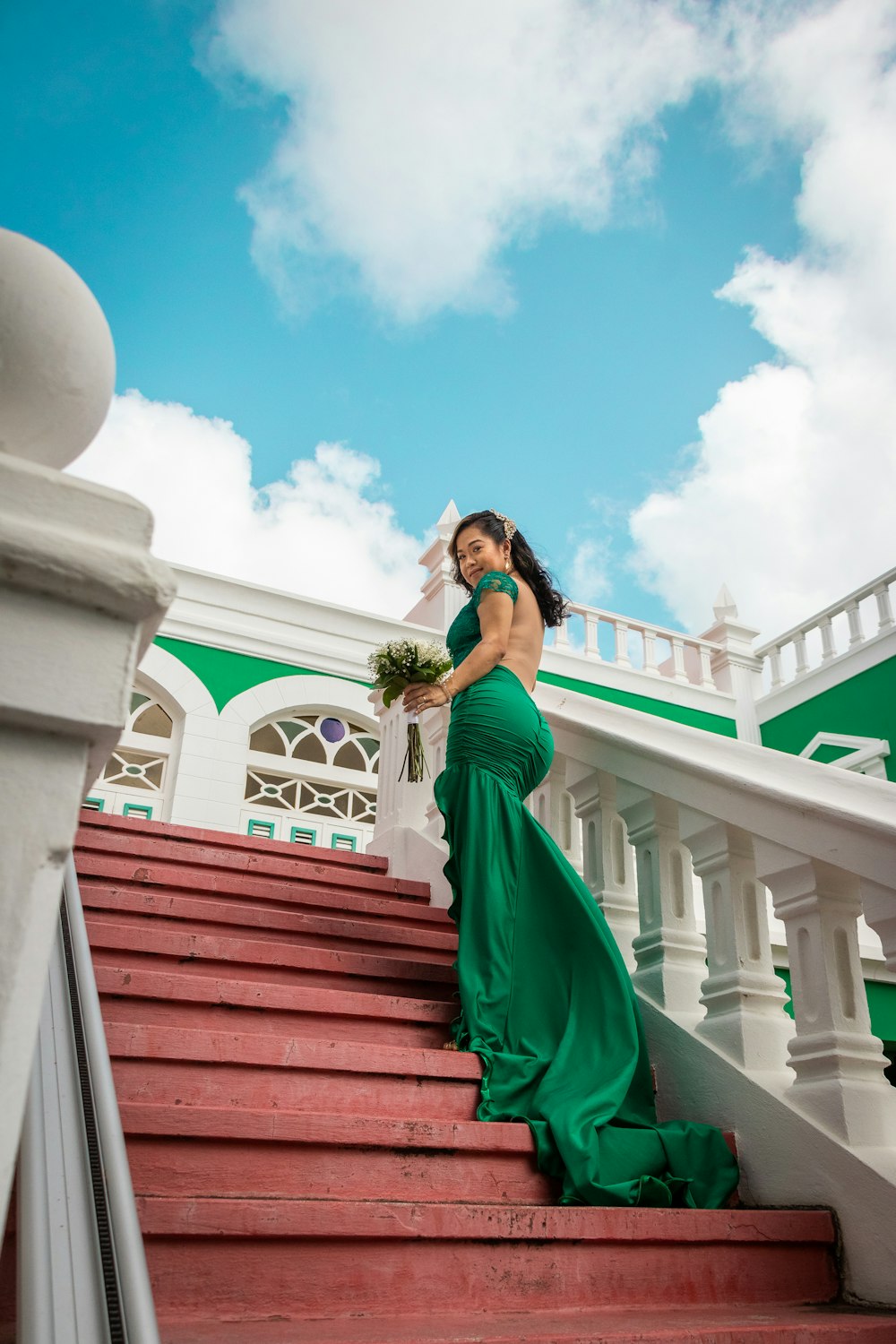 a beautiful woman in a green dress standing on some stairs