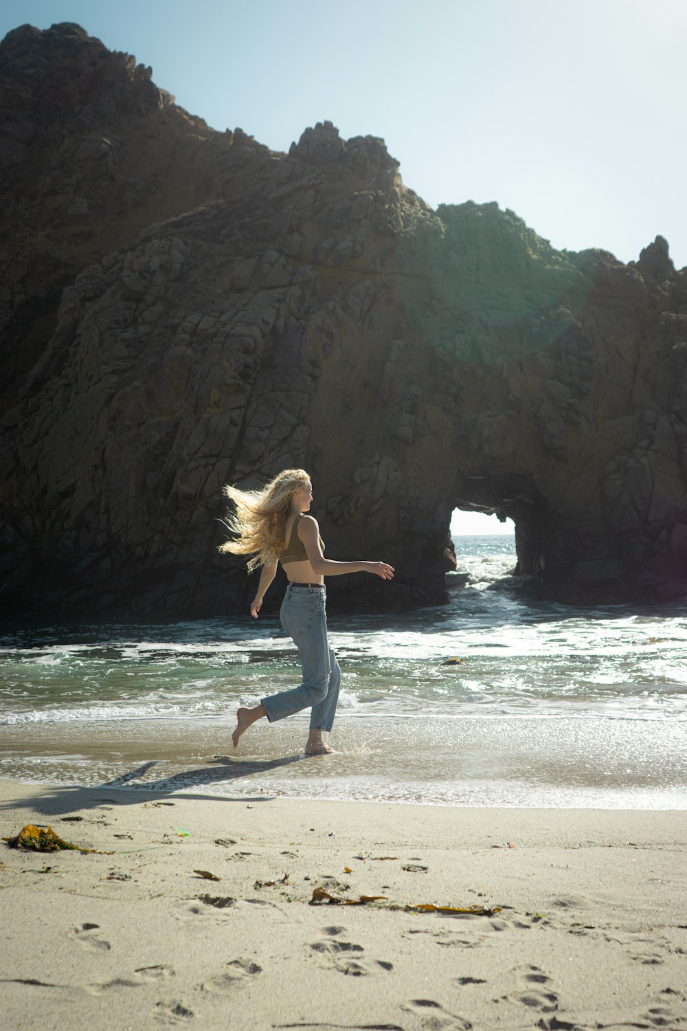 uma mulher correndo na praia perto de uma formação rochosa