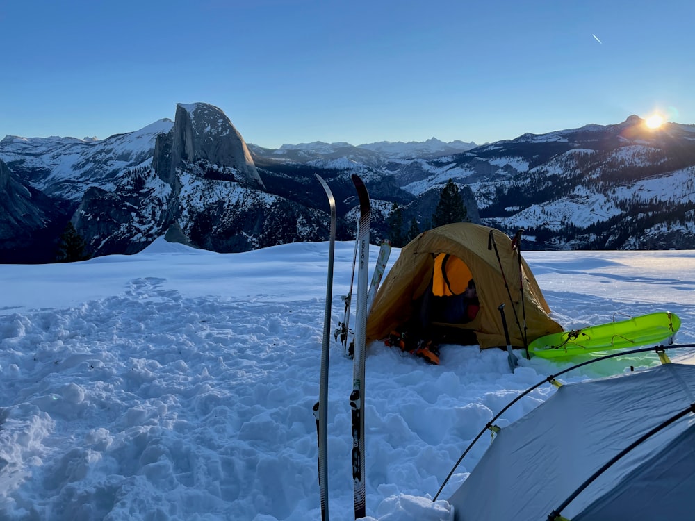 a tent and skis in the snow with mountains in the background