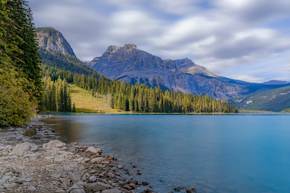 a lake surrounded by trees and mountains under a cloudy sky