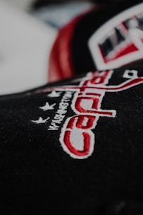 Embroidered text and design featuring the word 'Capitals' in red and white against a dark background. Stars and additional text are subtly visible above the main word.