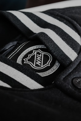 Black and white striped fabric with a close-up view of an NHL logo. The logo is situated on a tag or label, surrounded by dark fabric and a button.