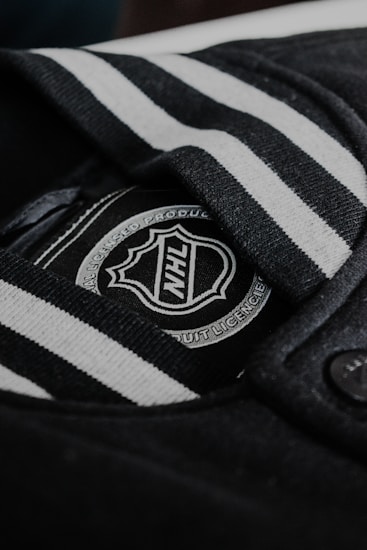 Black and white striped fabric with a close-up view of an NHL logo. The logo is situated on a tag or label, surrounded by dark fabric and a button.