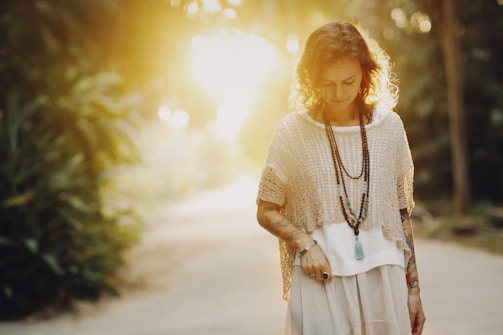 A cheerful person modeling layered outfits with hats and bracelets in natural sunlight.