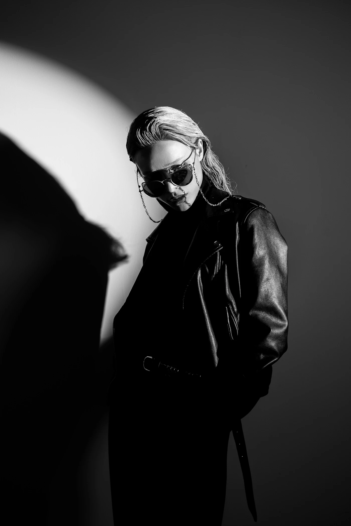Model in a black leather jacket and round sunglasses, lit by a single spotlight