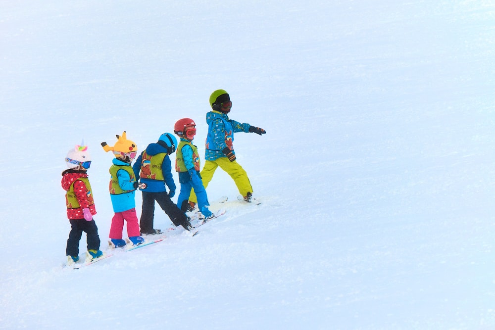 a group of young children riding skis down a snow covered slope