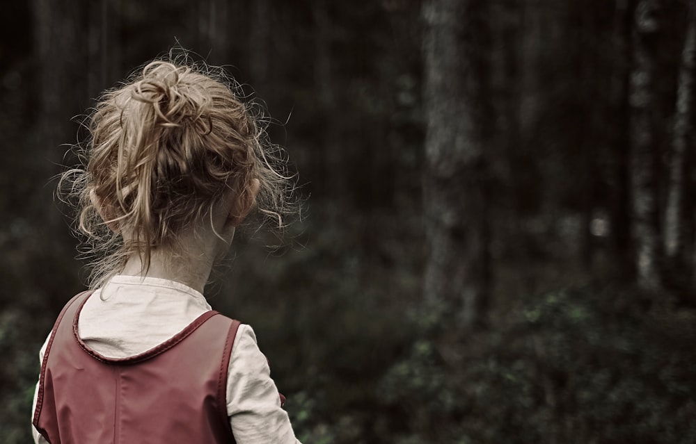 a woman in a red vest is walking through the woods