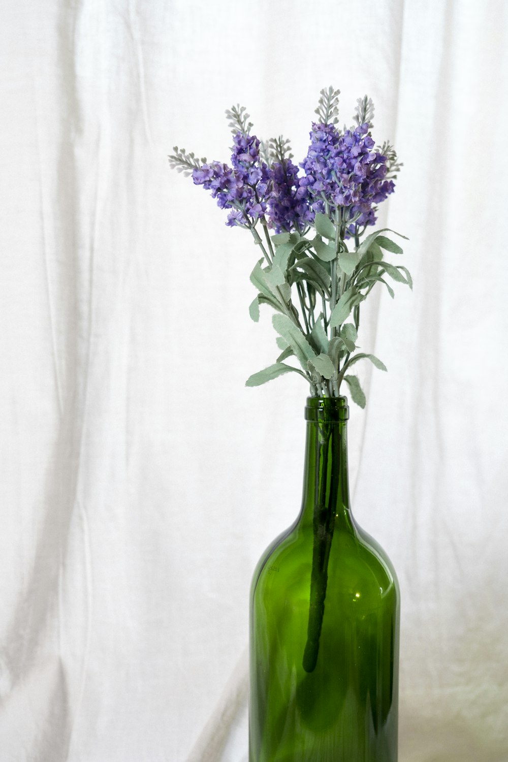 a green glass vase with purple flowers in it