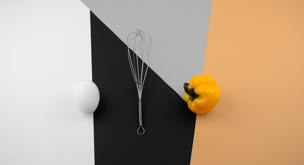 a whisk and a yellow pepper on a wall