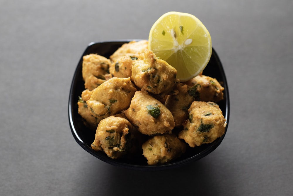 a black bowl filled with fried food and a lemon wedge