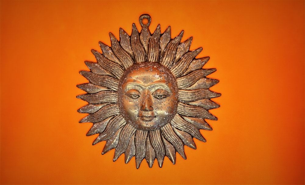 ein metallenes Sonnengesicht auf orangefarbenem Hintergrund