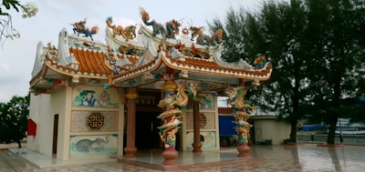An ornate, traditional Chinese-style temple with colorful dragons and mythical creatures decorating the roof. Intricate murals and patterns adorn the exterior walls, and the temple is set in a serene environment with trees and a body of water nearby.