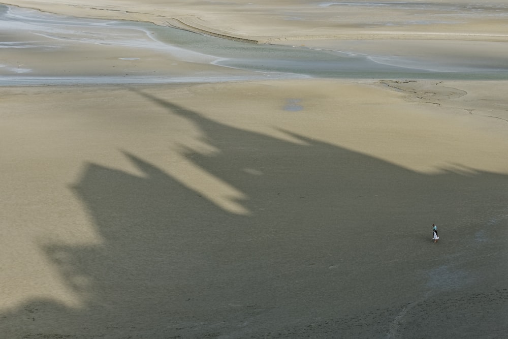 uma sombra de uma pessoa andando em uma praia