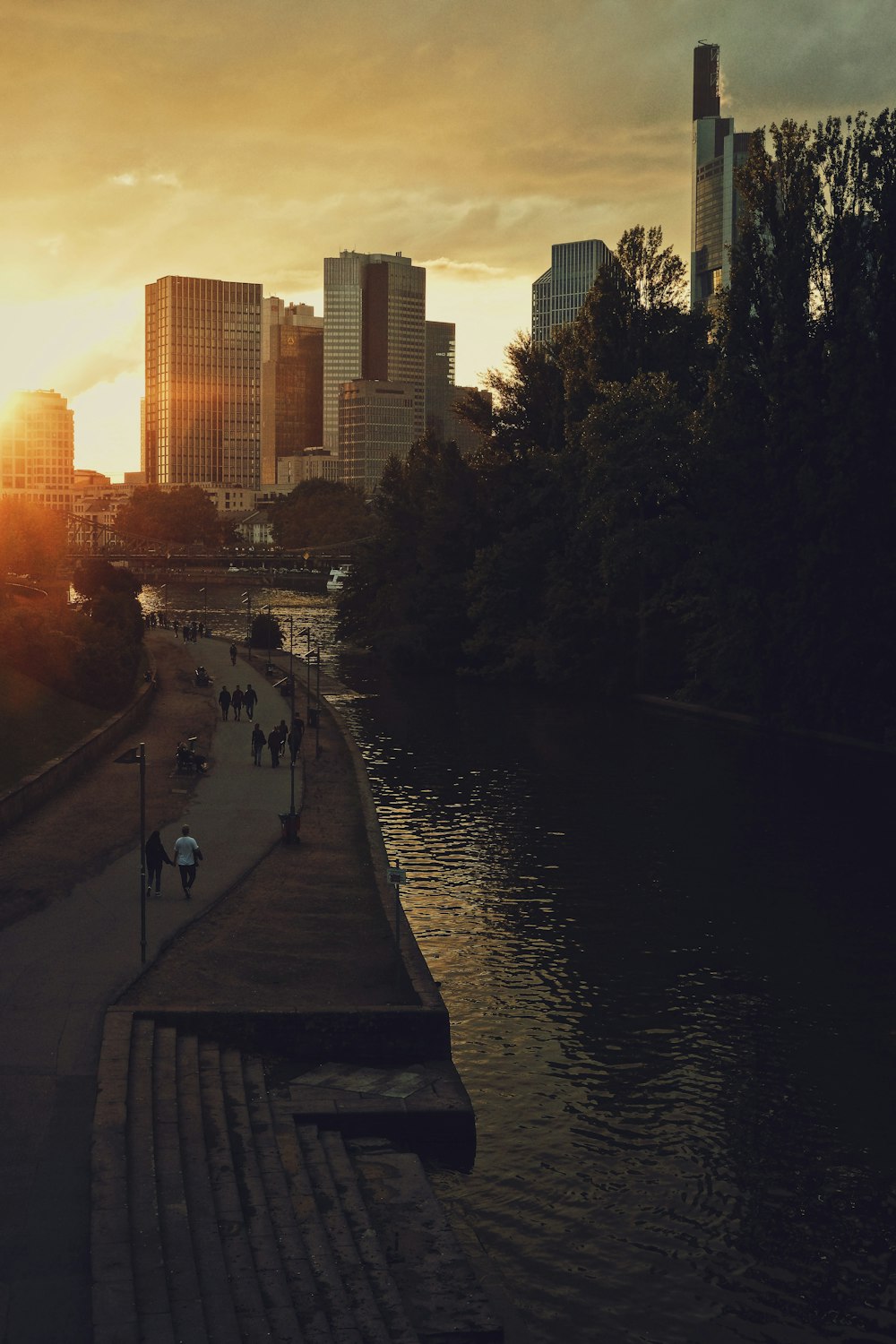 the sun is setting over a river with a city in the background