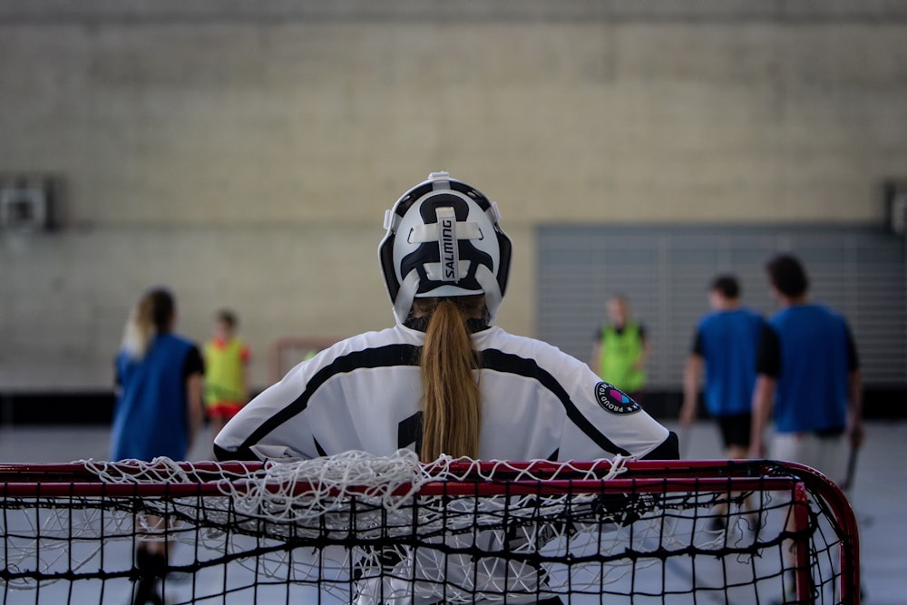 a girl in a white and black goalie suit sitting in front of a net