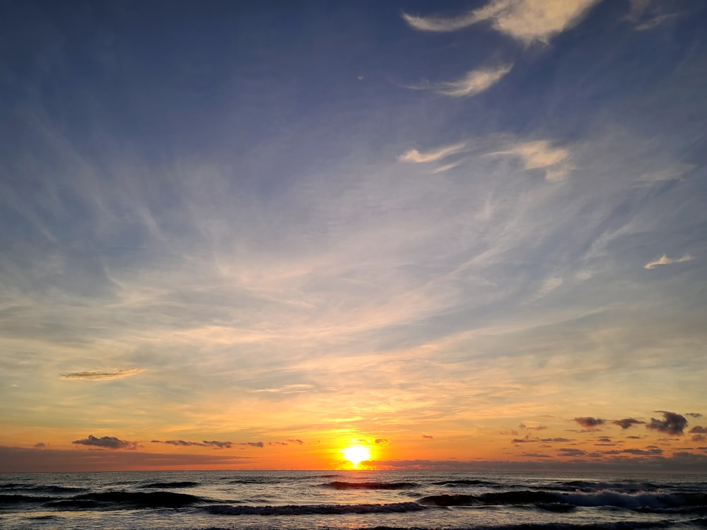 the sun is setting over the ocean on a cloudy day