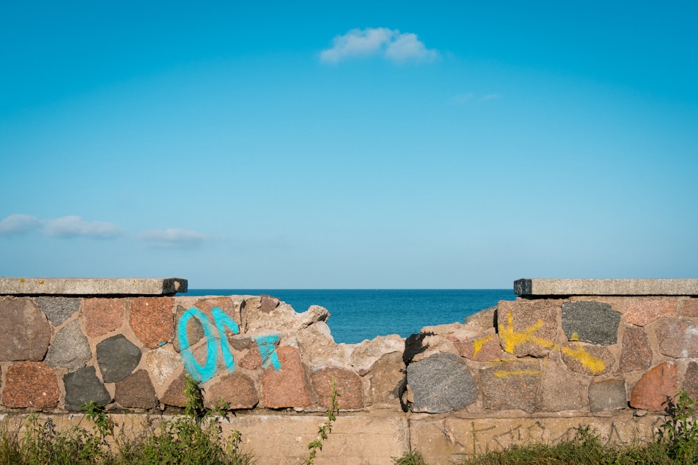 a stone wall with graffiti on it next to the ocean