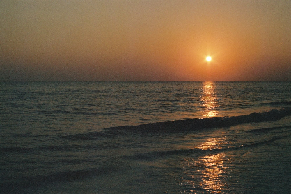 the sun is setting over the water at the beach