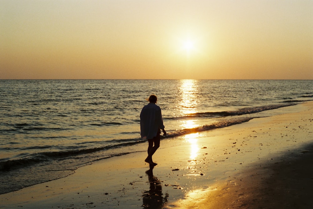 a man walking along the beach at sunset