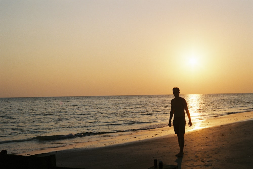 a man walking on the beach at sunset