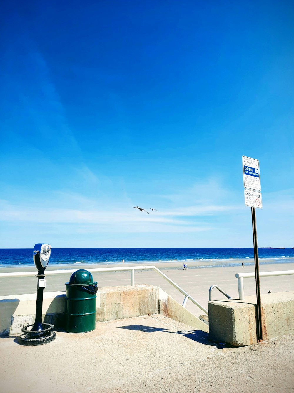 a street sign next to a trash can on a beach