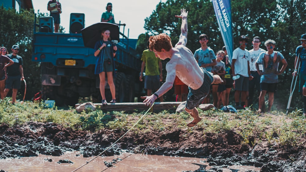 a shirtless man jumping into a muddy puddle