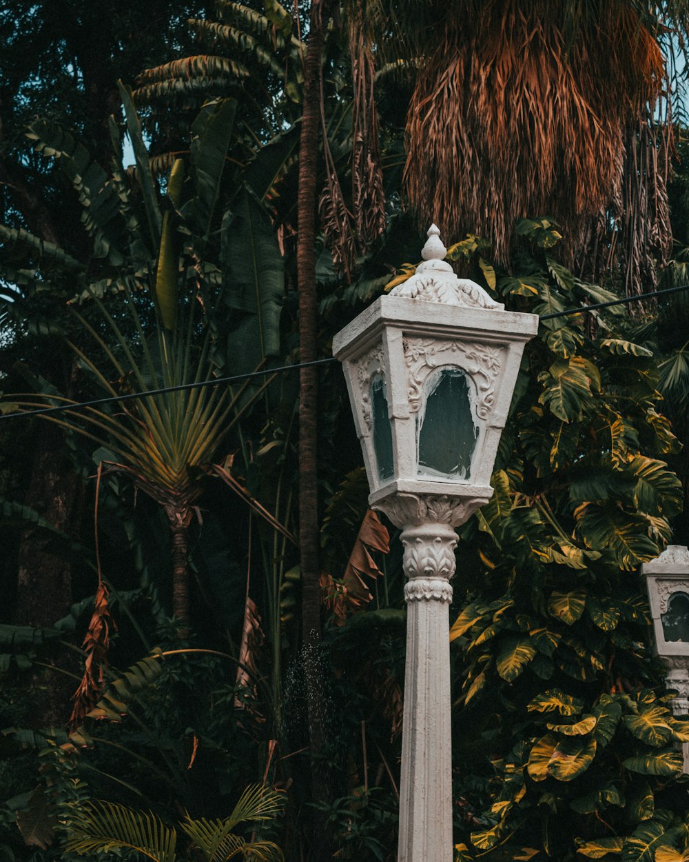 a white lamp post in front of some trees