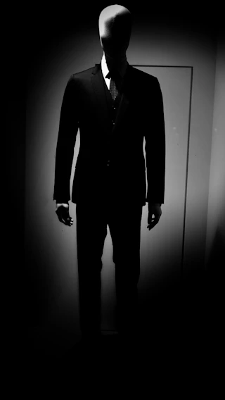 A sleek black mannequin dressed in a flowing beige unstitched suit fabric, softly lit against a minimalist backdrop.