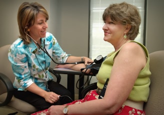 a woman with a stethoscope sitting next to a woman in a chair
