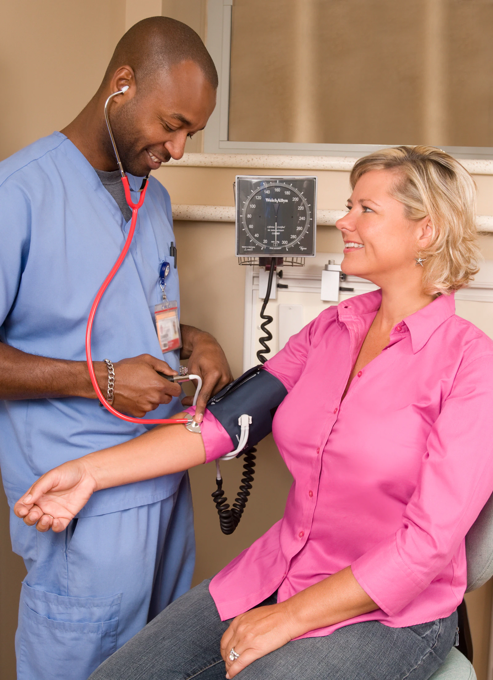 A healthcare worker in blue scrubs checking a patient's blood pressure