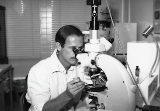 a black and white photo of a man looking through a microscope
