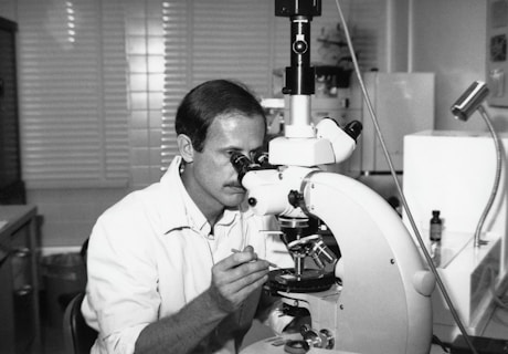 a black and white photo of a man looking through a microscope