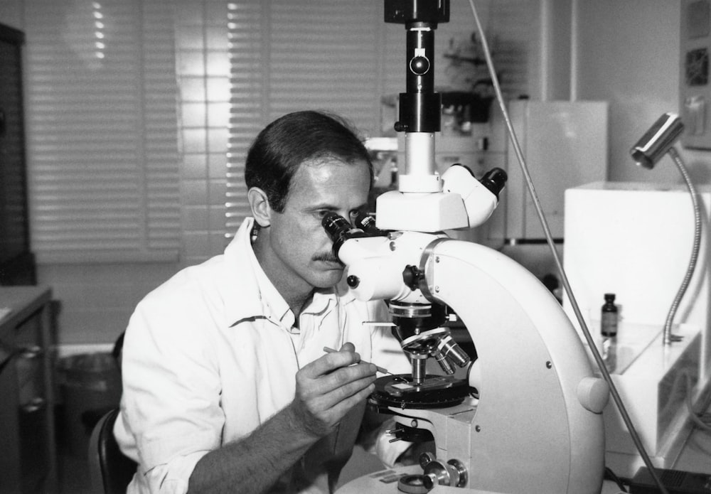 a black and white photo of a man looking through a microscope