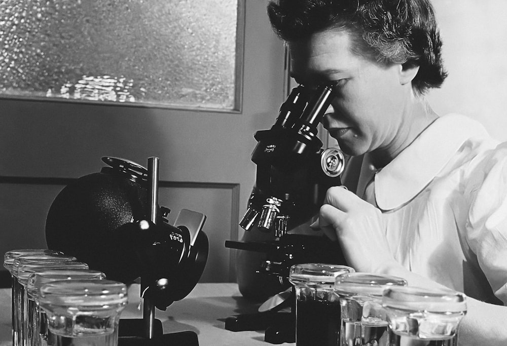 a woman looking through a microscope into jars