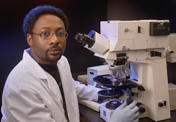 a man in a lab coat is looking into a microscope