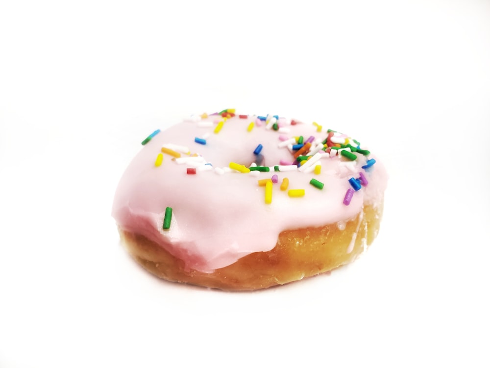 a pink frosted donut with sprinkles on a white background
