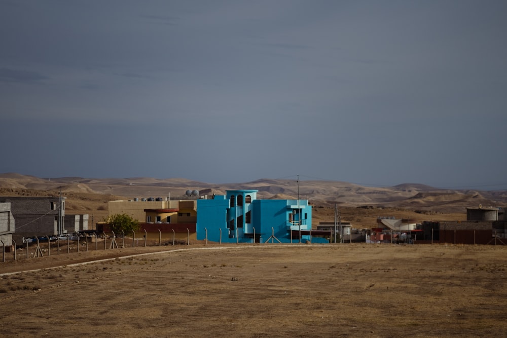 a blue building sitting in the middle of a dry grass field