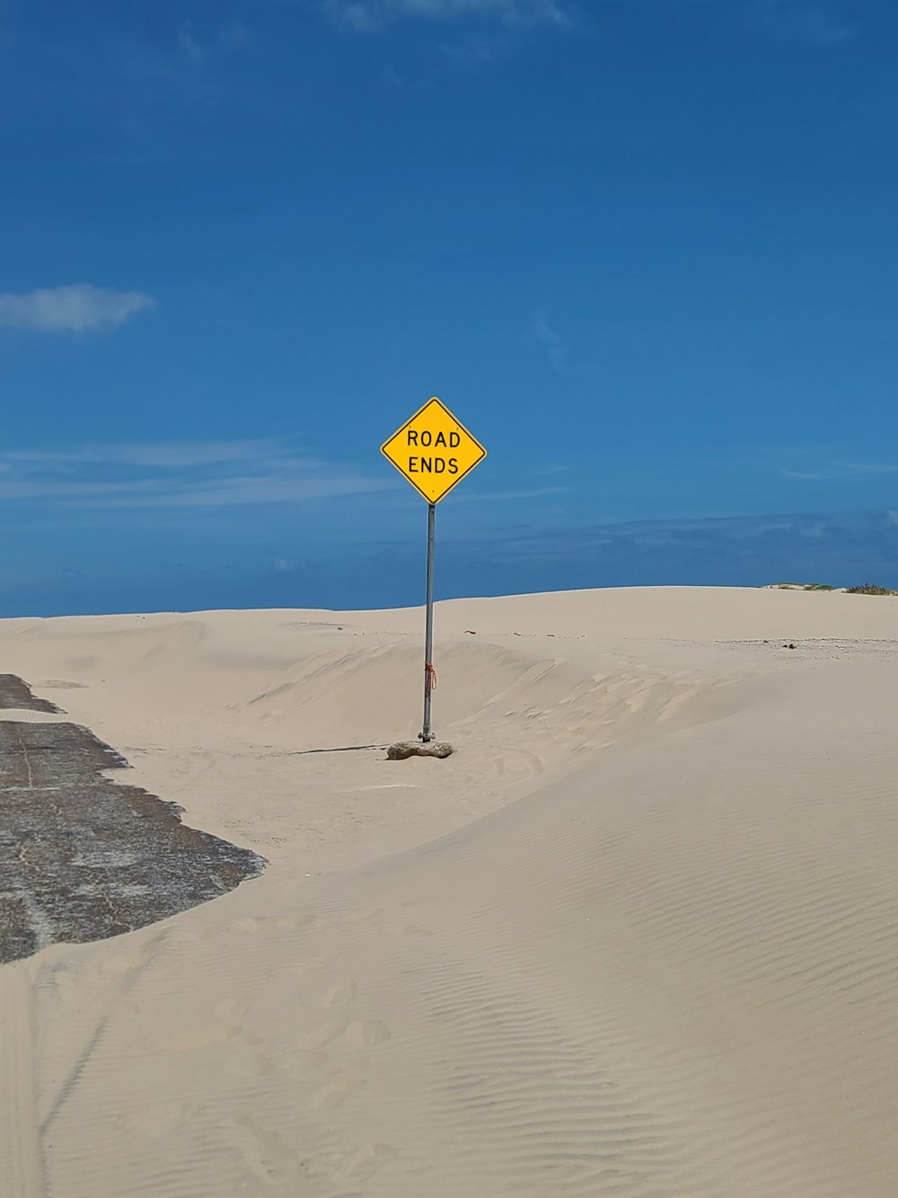 a yellow road sign sitting on top of a sandy beach