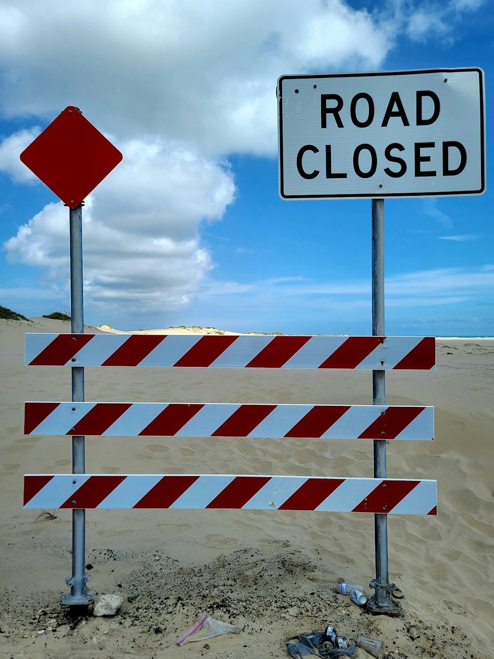 a road closed sign sitting on top of a sandy beach