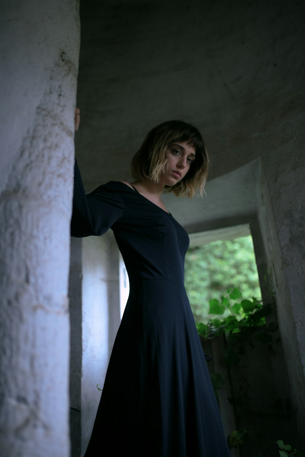 a woman in a black dress leaning against a wall