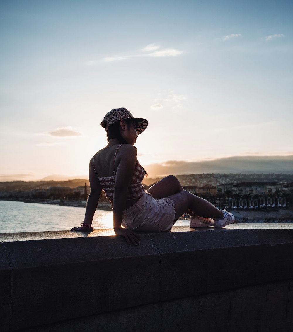 a woman sitting on a ledge looking at the water