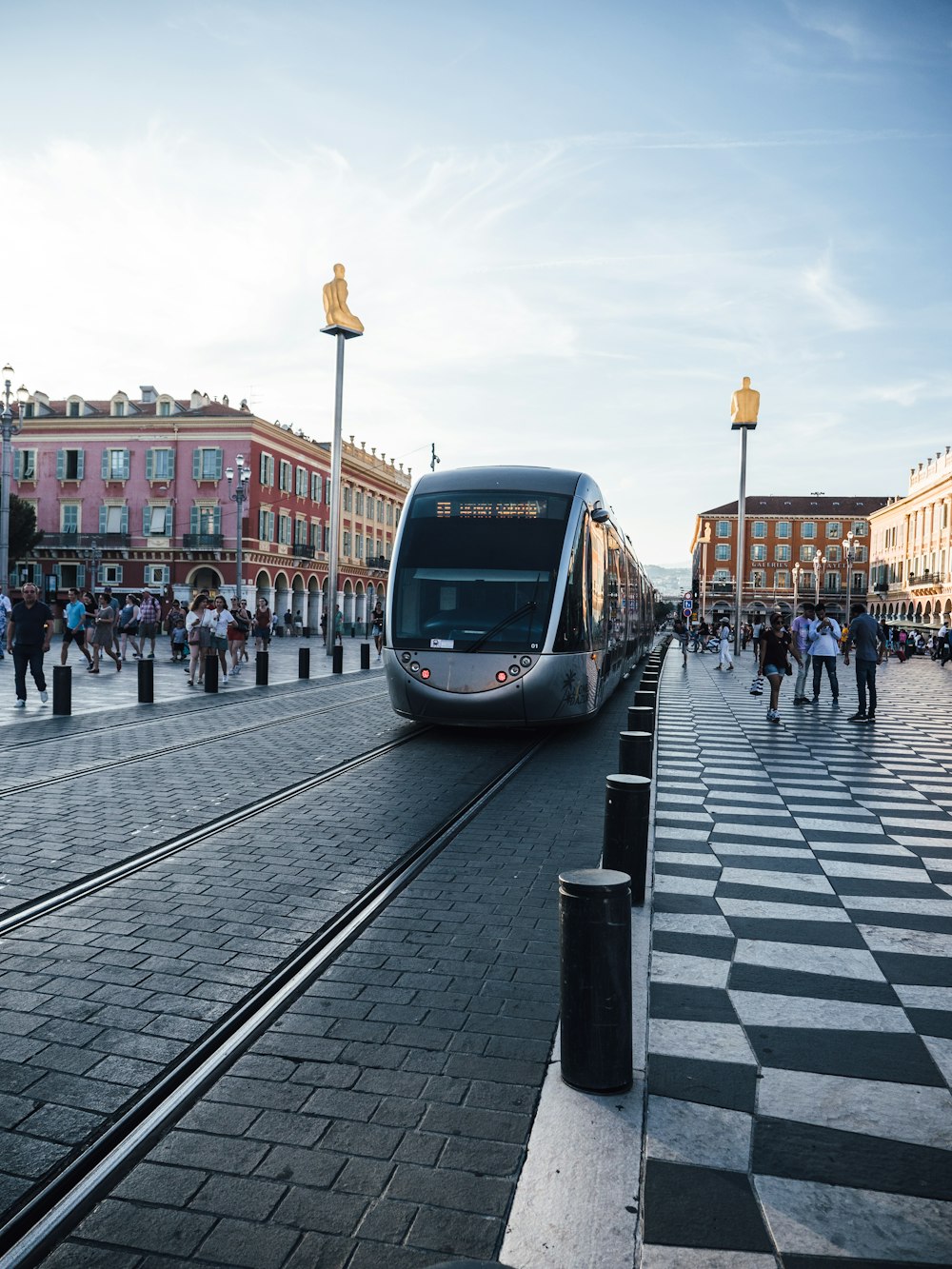 a silver train traveling down train tracks next to a crowd of people