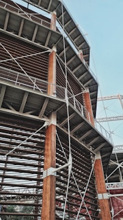 A large architectural structure featuring wooden beams and metal scaffolding. The design is intricate, with crisscrossing metal supports and a series of horizontal and vertical lines. The structure seems to be part of a larger construction, possibly a building or stadium.