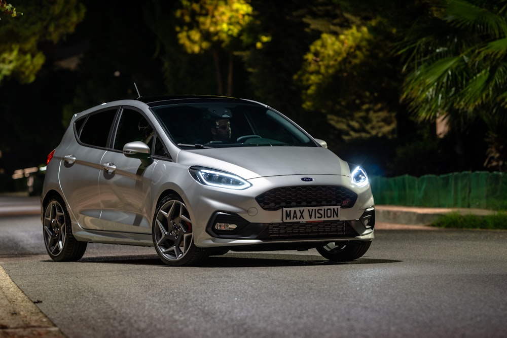 a silver car driving down a street at night