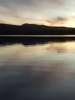 A calm lake reflecting a pastel-colored sky during early evening.
