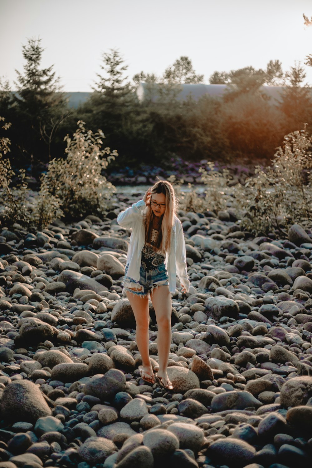 a woman standing on a rocky beach next to a forest