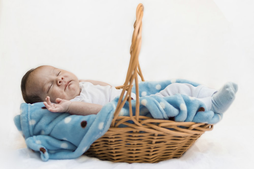 a baby sleeping in a basket with a blanket