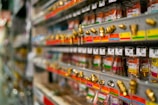 Rows of metal fittings and adapters are neatly arranged on display shelves in a store. Each item is attached to color-coded labels and price tags, giving a sense of organization and variety. The shelves extend into the background, suggesting a large selection of hardware items.
