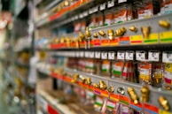 Rows of metal fittings and adapters are neatly arranged on display shelves in a store. Each item is attached to color-coded labels and price tags, giving a sense of organization and variety. The shelves extend into the background, suggesting a large selection of hardware items.