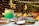 A richly decorated cake with layers of green and cream frosting is displayed on a cake stand surrounded by an assortment of desserts including cupcakes and cake pops. Soft lighting and a background adorned with strings of fairy lights and balloons create an elegant and festive atmosphere.